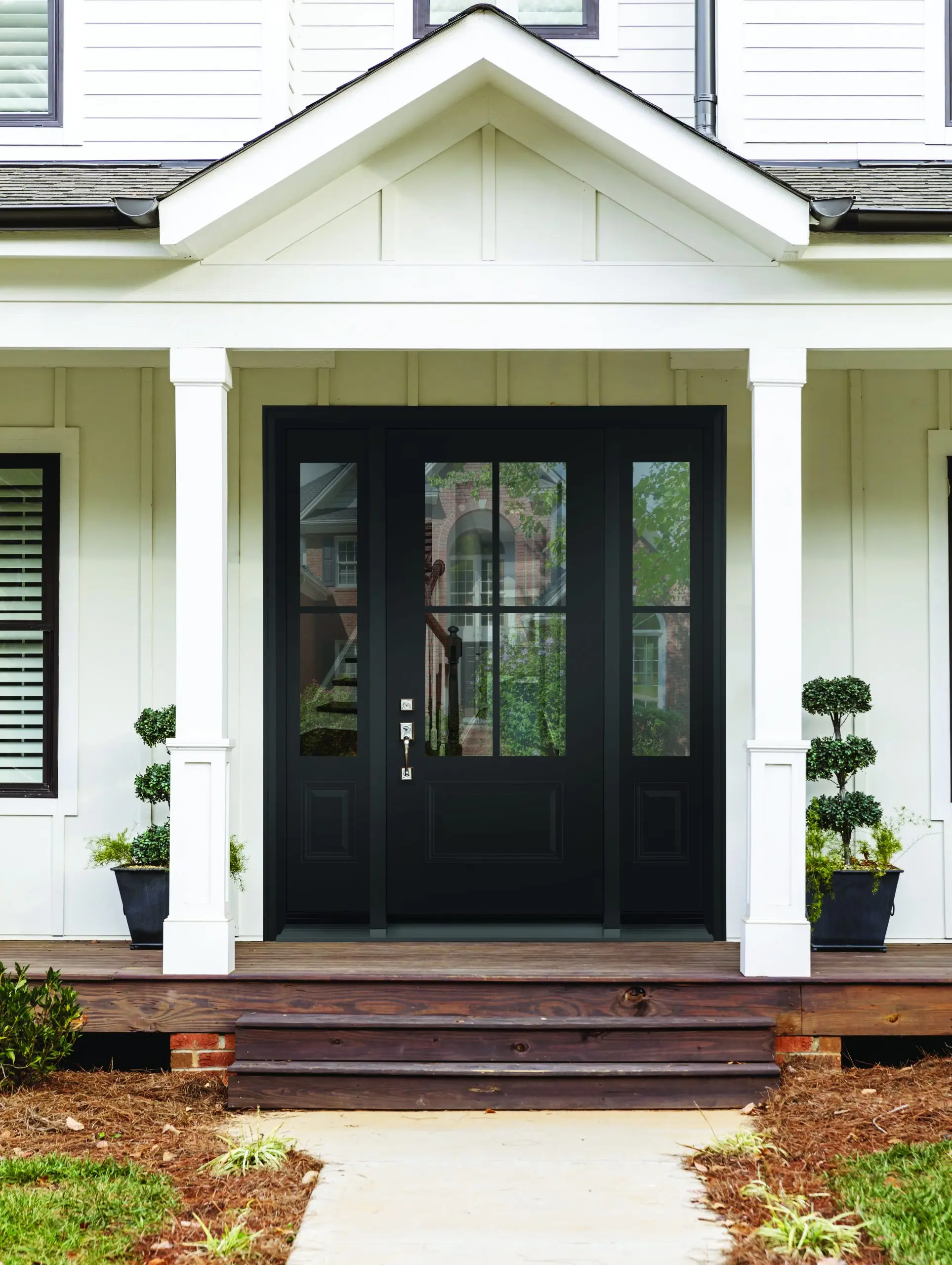 Front door/Exterior shot of a white house, nicely landscaped with a brown door with multiple windows